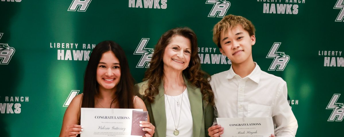 A woman smiles as she poses with a boy and a girl holding certificates.