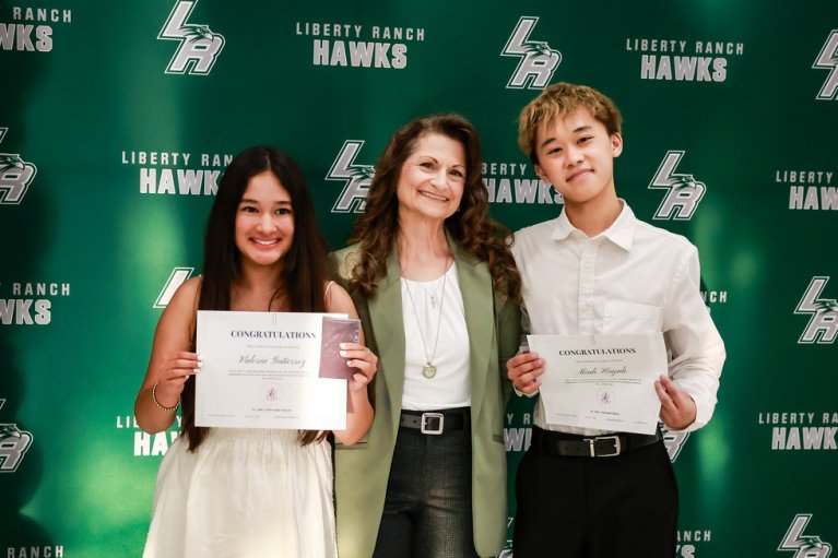 A woman smiles as she poses with a boy and a girl holding certificates.