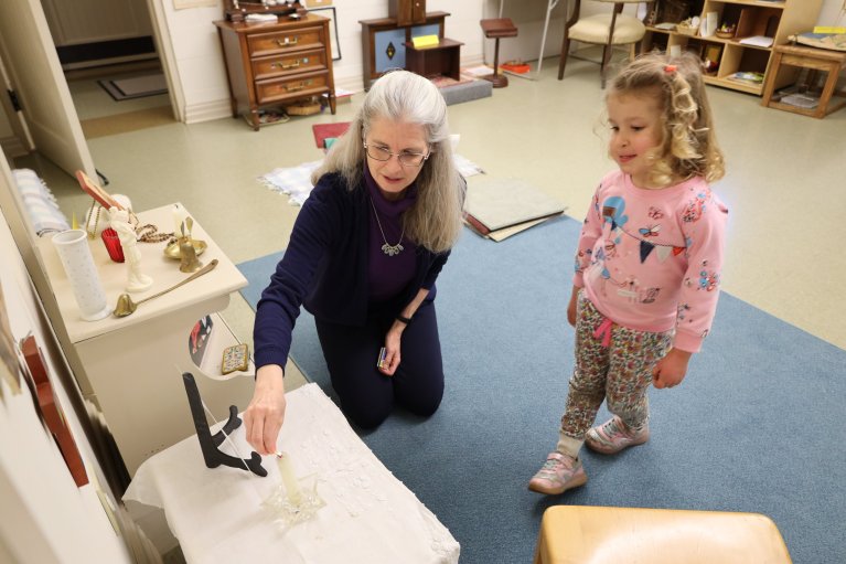 Catechist Shannon Townsend helps student Ruby light the altar candle.