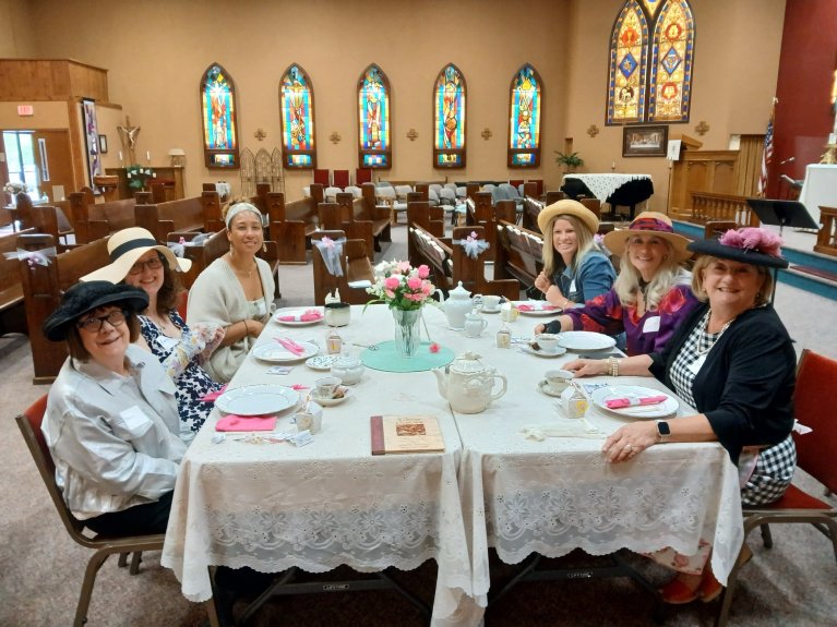 ladies in hats dressed up around a fancy tea setting