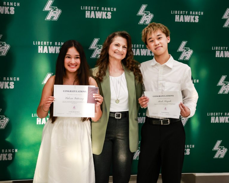 A woman smiles as she poses with a boy and a girl holding certificates.